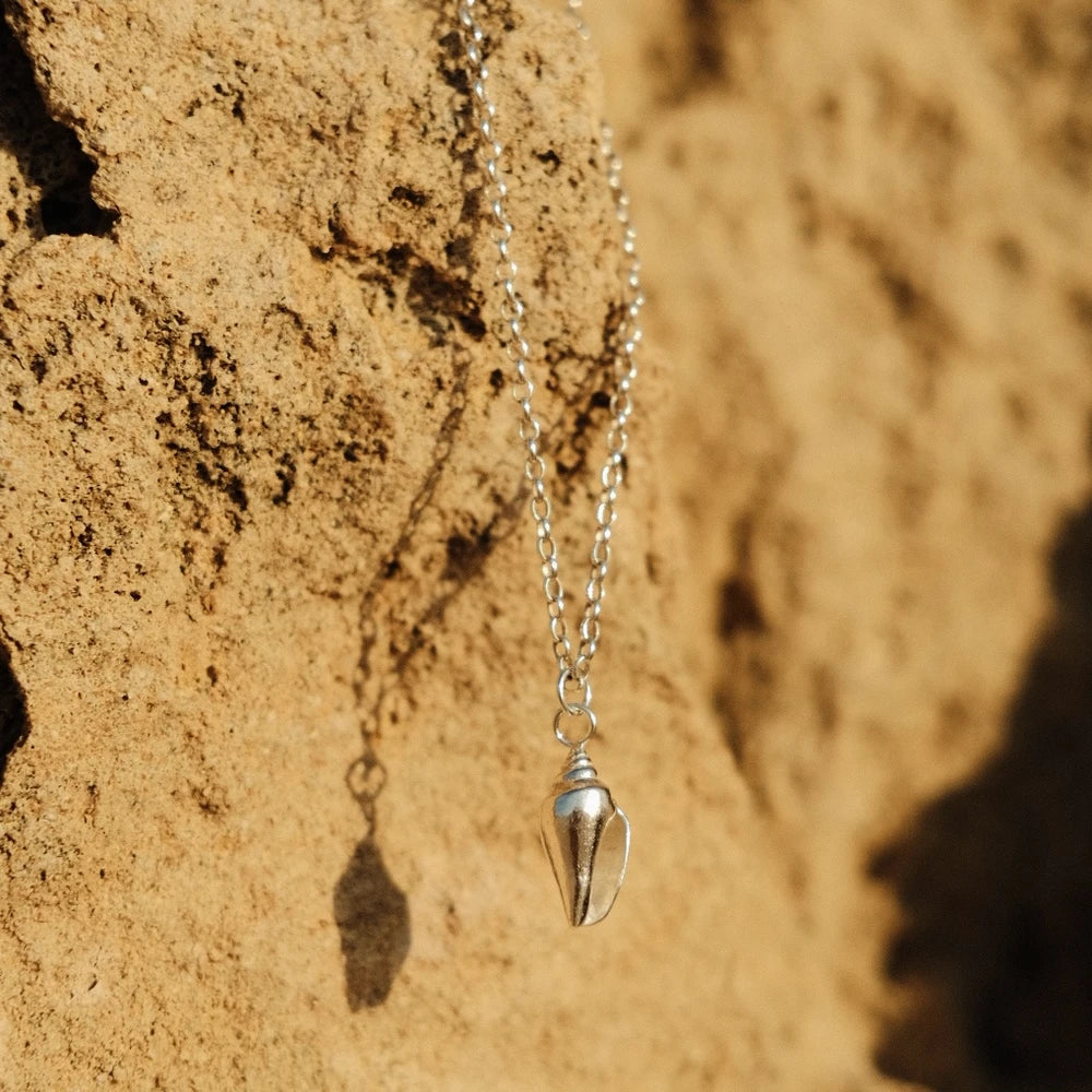 תקריב של תליון קונכייה עשוי כסף סטרלינג על רקע חול ים, משקף עיצוב אלגנטי ועל-זמני.