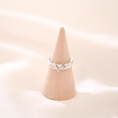 טבעת כסף סטרלינג טריו מוצגת על מעמד עץ, מדגישה את המבנה המינימליסטי והתנועה העדינה של החישוקים.