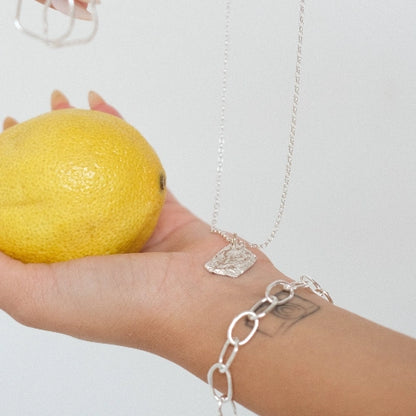 שרשרת כסף 925 'אש' עם תליון בטקסטורת רטיקולציה ייחודית, מונחת על כף יד לצד לימון רענן בעיצוב עבודת יד של Shiroo.