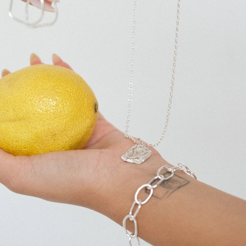 שרשרת כסף 925 'אש' עם תליון בטקסטורת רטיקולציה ייחודית, מונחת על כף יד לצד לימון רענן בעיצוב עבודת יד של Shiroo.