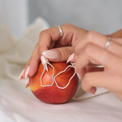 עגילי כסף סטרלינג אסימטריים מונחים על פרי, מדגישים את הקווים האורגניים והזורמים של התכשיט בעבודת צורפות אישית.