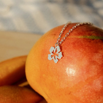 תליון פרח היביסקוס מכסף סטרלינג מונח על פרי כתום, מדגיש את העיצוב האורגני והטבעי של התכשיט.