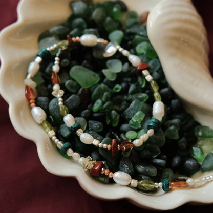 תקריב של אבני חן טבעיות ופנינים בשרשרת כסף מעוצבת, המדגיש את הטקסטורות והצבעוניות העשירה של אבני הטורקיז והפרידוט.