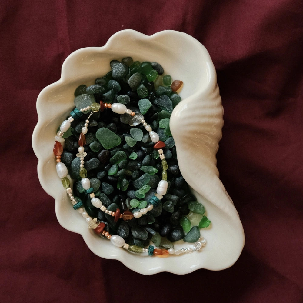 שרשרת פנינים ואבני חן צבעוניות מונחת בתוך קונכייה דקורטיבית, תכשיט אמירה יוקרתי ומלא חיים בעיצוב אישי.