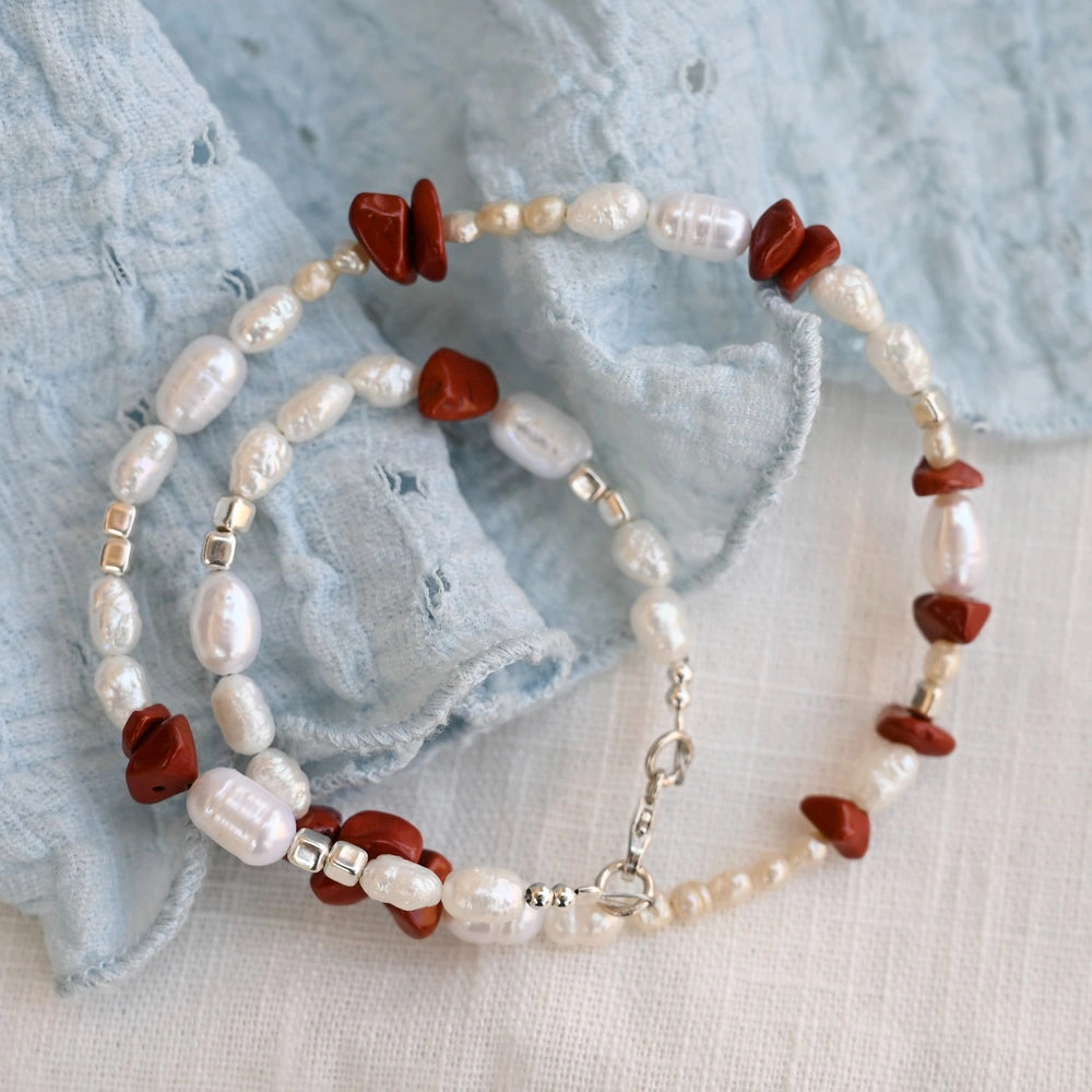 שרשרת כסף עם פנינים לבנות ואבני ג'ספר אדומות על רקע בד תכלת, שילוב צבעים קלאסי ונועז לקולקציית הקיץ של שירו.