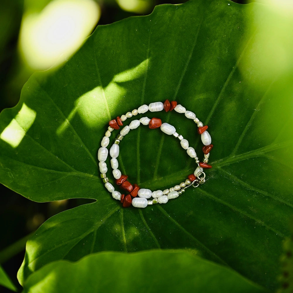 שרשרת פנינים ואבני חן ג'ספר אדומה מונחת על עלה טבעי, תכשיט אמירה בעבודת יד עם סוגר כסף איכותי.