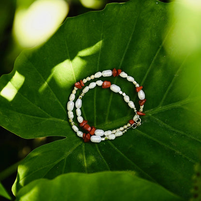 שרשרת פנינים ואבני חן ג'ספר אדומה מונחת על עלה טבעי, תכשיט אמירה בעבודת יד עם סוגר כסף איכותי.