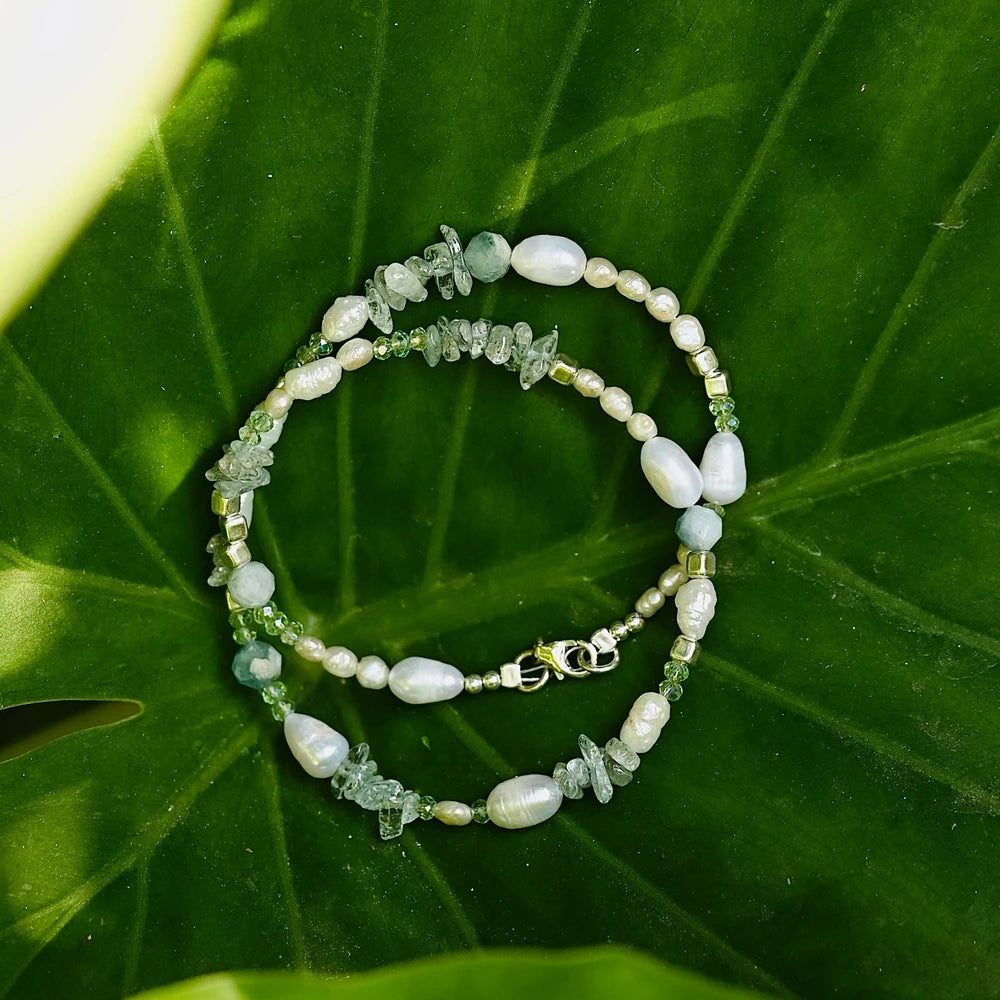 שרשרת פנינים ואבני חן אקוווה מרין מונחת על עלה ירוק גדול, תכשיט בהשראת הטבע עם סוגר כסף איכותי.