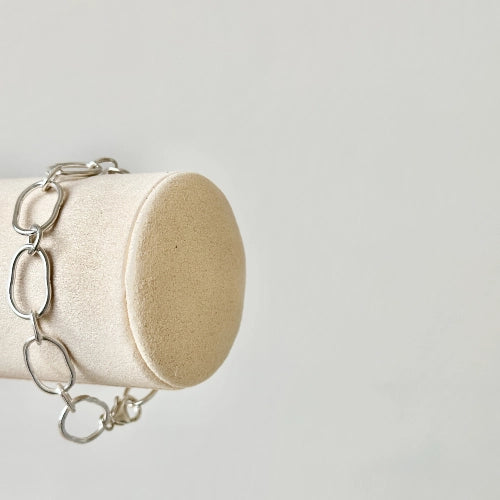 צמיד כסף שירו מוצג על מעמד גלילי, מדגיש את השילוב בין לולאות גדולות וקטנות ליצירת מראה אופנתי וייחודי.