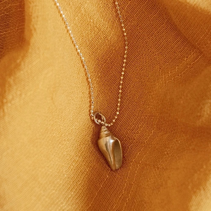 מבט מקרוב על תליון קונכייה מכסף 925 על רקע בד צהוב, המדגיש את הפרטים הקטנים והגימור המוקפד.