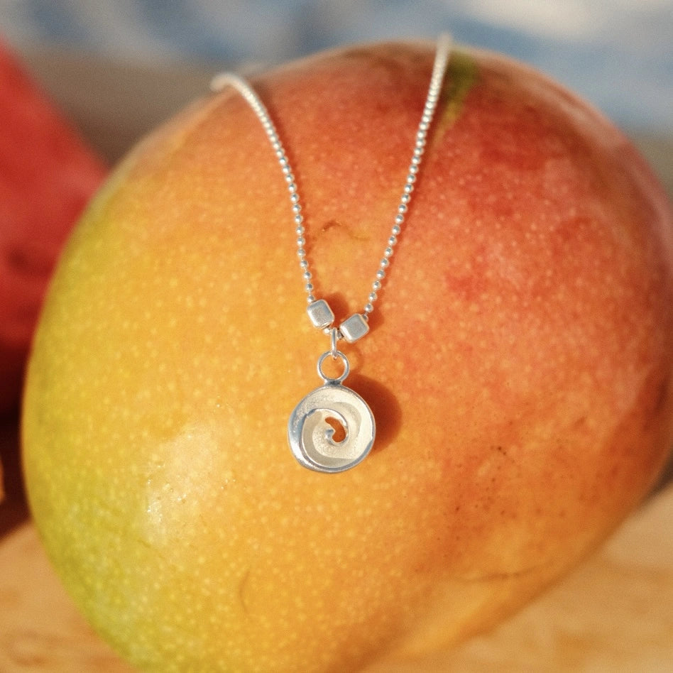 תליון כסף 'עין הים' מונח על מנגו רענן, משקף את האופי הקיצי והצבעוני של קולקציית התכשיטים החדשה.