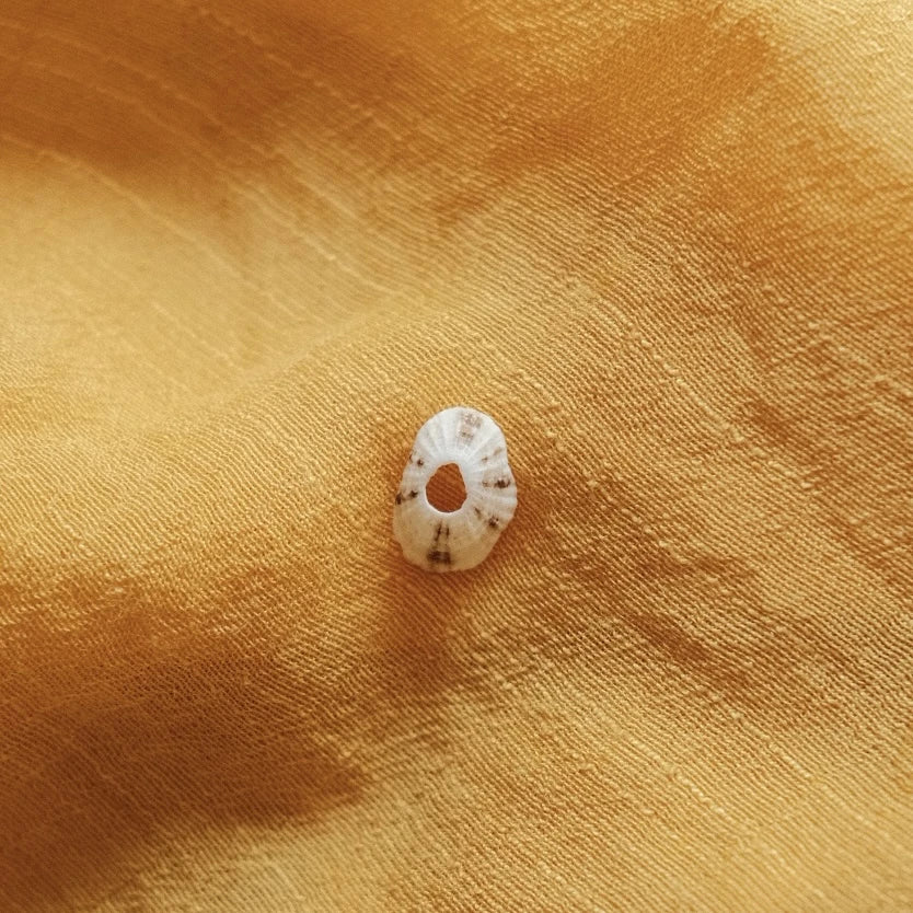 מבט מקרוב על תליון צדף מכסף סטרלינג על רקע בד צהוב, המדגיש את הטקסטורה הייחודית והחור המרכזי.