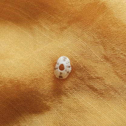 מבט מקרוב על תליון צדף מכסף סטרלינג על רקע בד צהוב, המדגיש את הטקסטורה הייחודית והחור המרכזי.