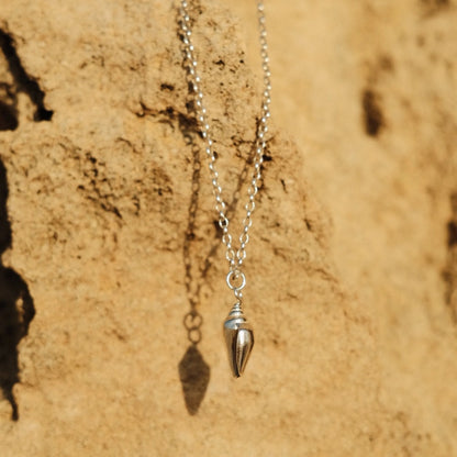 תליון קונכייה מכסף סטרלינג על שרשרת עדינה מונח על סלע חולי, תכשיט בהשראת עולם הים והחופים.