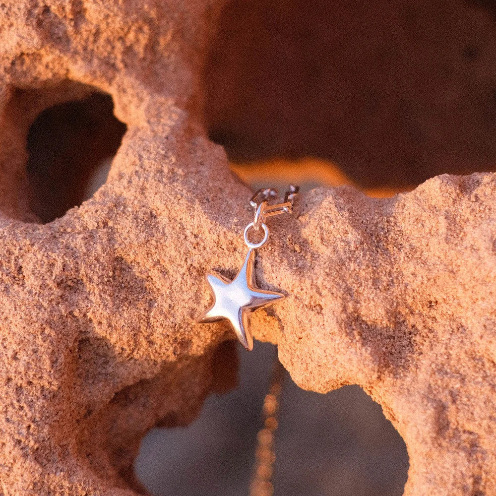 תליון כוכב ים מכסף סטרלינג מונח על סלע טבעי, מדגיש את ההשראה של שירו מהחוף והים.