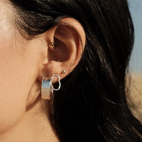 עגילי כסף 925 בריקוע עגול בעבודת יד על אוזן לקוחה, מראה אלגנטי וייחודי המשלב טקסטורה אורגנית.