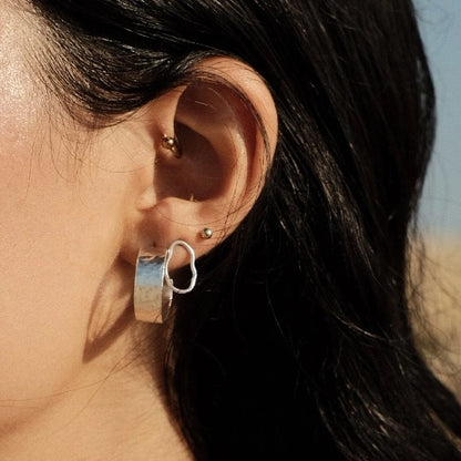 עגילי כסף 925 בריקוע עגול בעבודת יד על אוזן לקוחה, מראה אלגנטי וייחודי המשלב טקסטורה אורגנית.