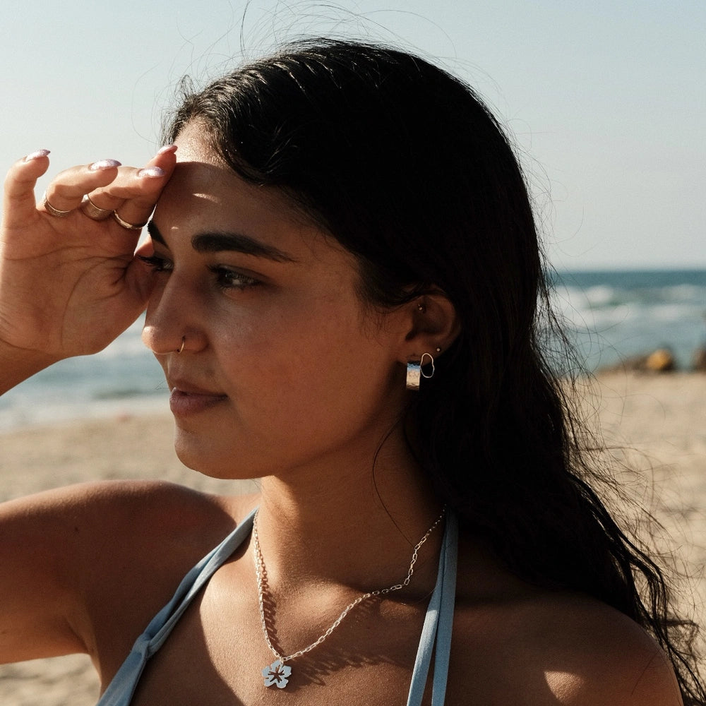 דוגמנית עונדת עגילי כסף מרוקעים בעיצוב עגול על רקע חוף הים, תכשיט מושלם למראה קיצי וטבעי.