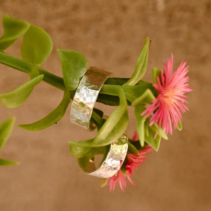 עגילי כסף בעיצוב ריקוע עגול תלויים על ענף עם פריחה ורודה, מדגישים את החיבור של Shiroo Jewelry לטבע.