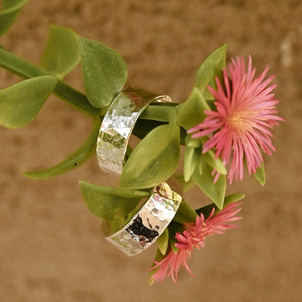 מבט מקרוב על טקסטורת הריקוע של עגילי הכסף על רקע פרחי גינה צבעוניים.