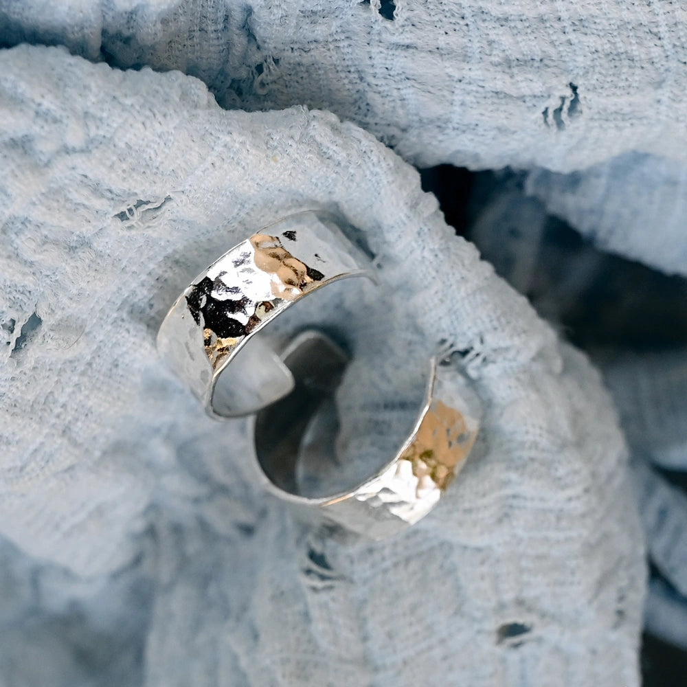 זוג עגילי חישוק רחבים מכסף סטרלינג עם ריקוע עגול מנצנץ, מונחים על רקע בד טקסטיל תכלת.