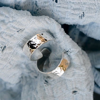 זוג עגילי חישוק רחבים מכסף סטרלינג עם ריקוע עגול מנצנץ, מונחים על רקע בד טקסטיל תכלת.