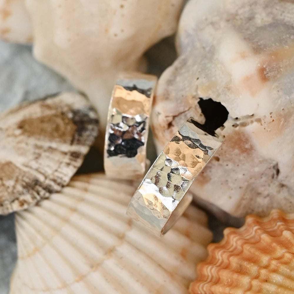 עגילי כסף עגולים מרוקעים מונחים על אוסף צדפים טבעיים, משקפים את השראת הים והחופש.