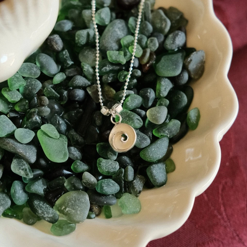 שרשרת כסף עם תליון עין הים בתוך קונכייה דקורטיבית מלאה באבנים ירוקות, מראה אורגני ויוקרתי.