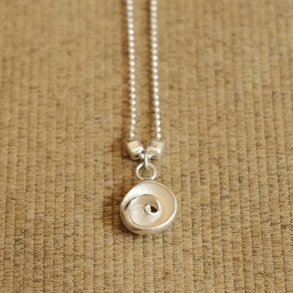 תקריב של שרשרת כסף עדינה עם תליון עין הים, תכשיט אלגנטי המתאים למראה יומיומי או כפריט נלווה לערב.