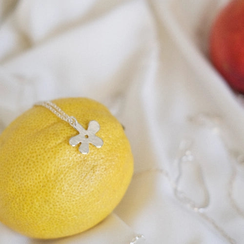 שרשרת כסף 925 עם תליון פרח בעיצוב חופשי וזורם בסגנון 'בוב ספוג', מונחת על לימון רענן כחלק מקולקציית הקיץ של Shiroo.