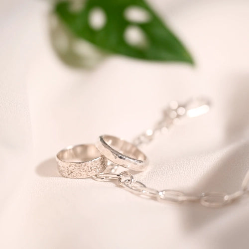 זוג טבעות כסף מרוקעות בעיצוב נקי ואלגנטי מונחות לצד עלה, תכשיט אמירה בעל נוכחות עדינה מסטודיו Shiroo.