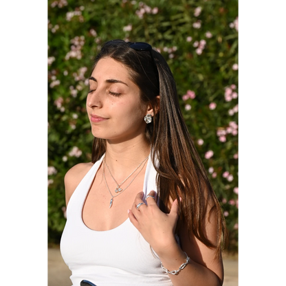 עגילי כסף יוליה של SHIROO, תמונת פנים מלאה של הדוגמנית על רקע פרחים ורודים. בשילוב שרשרות כסף שכבות, טבעות כסף ועל פרק ידה צמיד כסף. עגילי כסף סטרלינג 925 תוצרת ישראל.