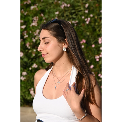 עגילי כסף יוליה של SHIROO, פרופיל צד של הדוגמנית עם משקפי שמש על הראש על רקע פרחים ורודים. בסטיילינג עם שרשרות כסף שכבות וצמיד כסף חוליות. עגילי כסף 925 עיצוב ישראלי.