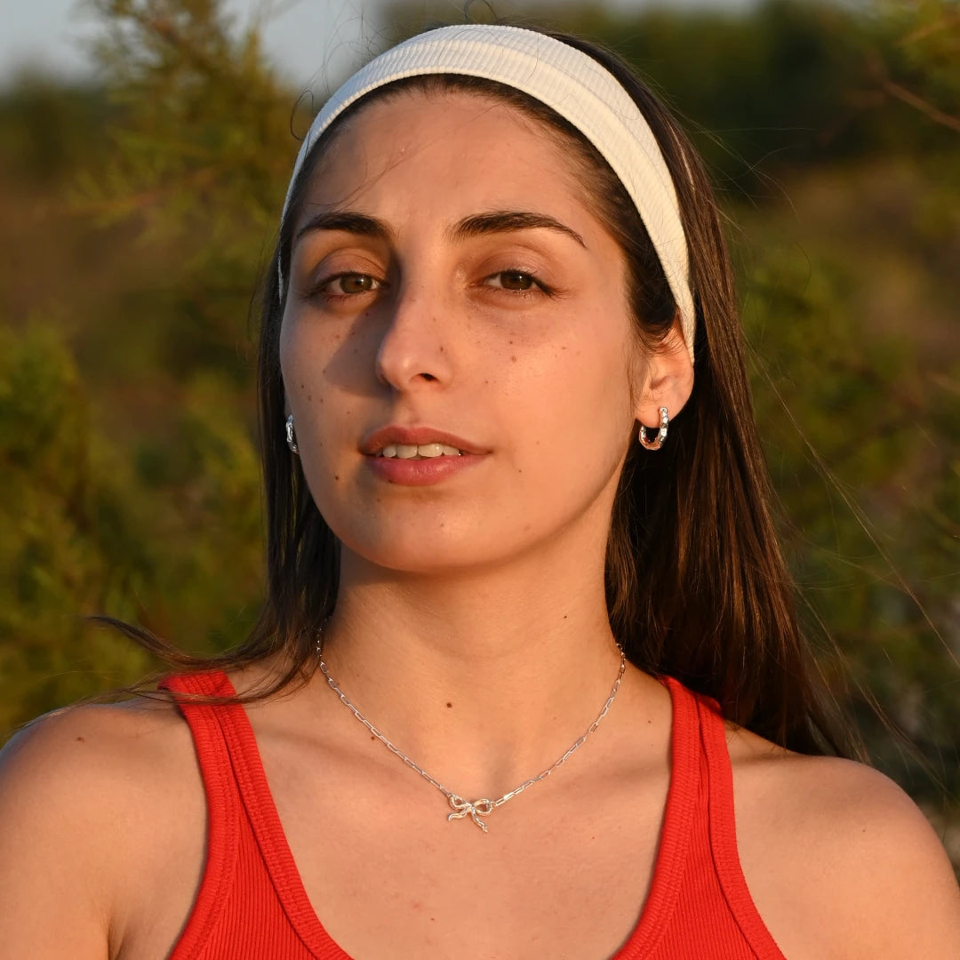 עגיל כסף חישוק קצר של SHIROO, מוצג על שתי האוזניים של הדוגמנית בתמונת פנים באור שקיעה זהוב. סטיילינג עם שרשרת כסף עדינה עם תליון פרפר על רקע טבע ירוק. עגיל כסף 925 עבודת יד תוצרת ישראל, זמין גם בכסף מצופה זהב.