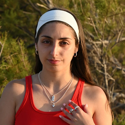 עגיל כסף חישוק ארוך של SHIROO על אוזן דוגמנית ברונטית עם כובע לבן ומבט ישיר למצלמה, על רקע טבע בשקיעה. בשילוב שרשרות כסף שכבות וטבעות כסף. עגיל כסף 925 עבודת יד תוצרת ישראל.