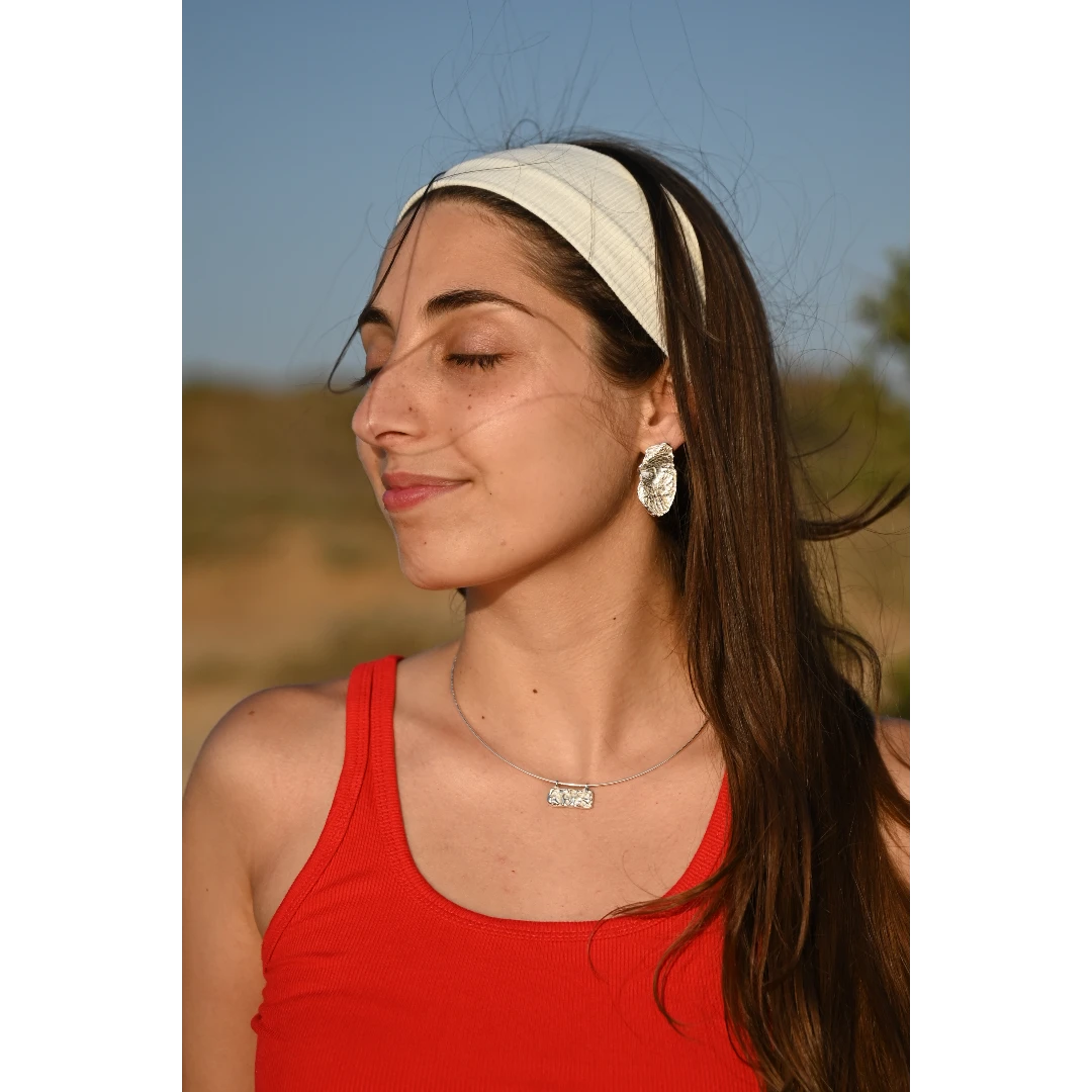 עגילי כסף מילאנו של SHIROO, תמונת פנים של הדוגמנית מביטה הצידה על רקע שמיים כחולים. בשילוב שרשרת כסף עם תליון אורגני. עגילי כסף 925 עבודת יד תוצרת ישראל.