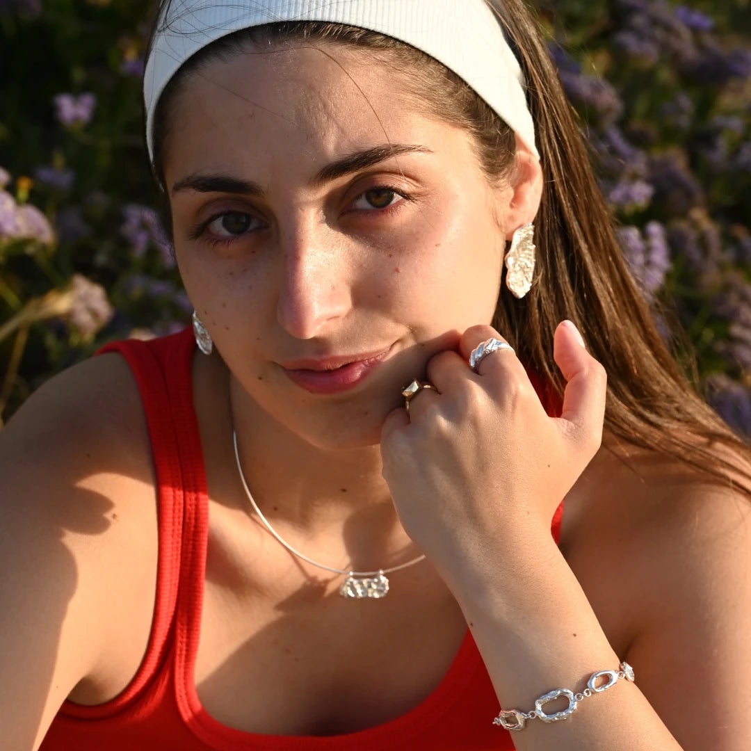 דוגמנית עונדת שרשרת כסף גלים לרוחב SHIROO על צ'וקר קשיח בשילוב עגילי כסף אורגניים – שדה פרחים ישראלי, אור שקיעה זהוב. סט תכשיטי כסף לאישה