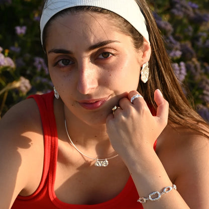 דוגמנית עונדת שרשרת כסף גלים לרוחב SHIROO על צ'וקר קשיח בשילוב עגילי כסף אורגניים – שדה פרחים ישראלי, אור שקיעה זהוב. סט תכשיטי כסף לאישה
