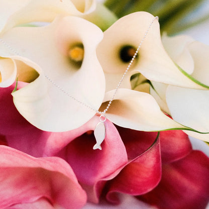 שרשרת דג כסף 925 עם תליון מינימליסטי מונחת בתוך פרחי קאלה ורודים ולבנים, עיצוב עדין בעבודת יד של Shiroo.